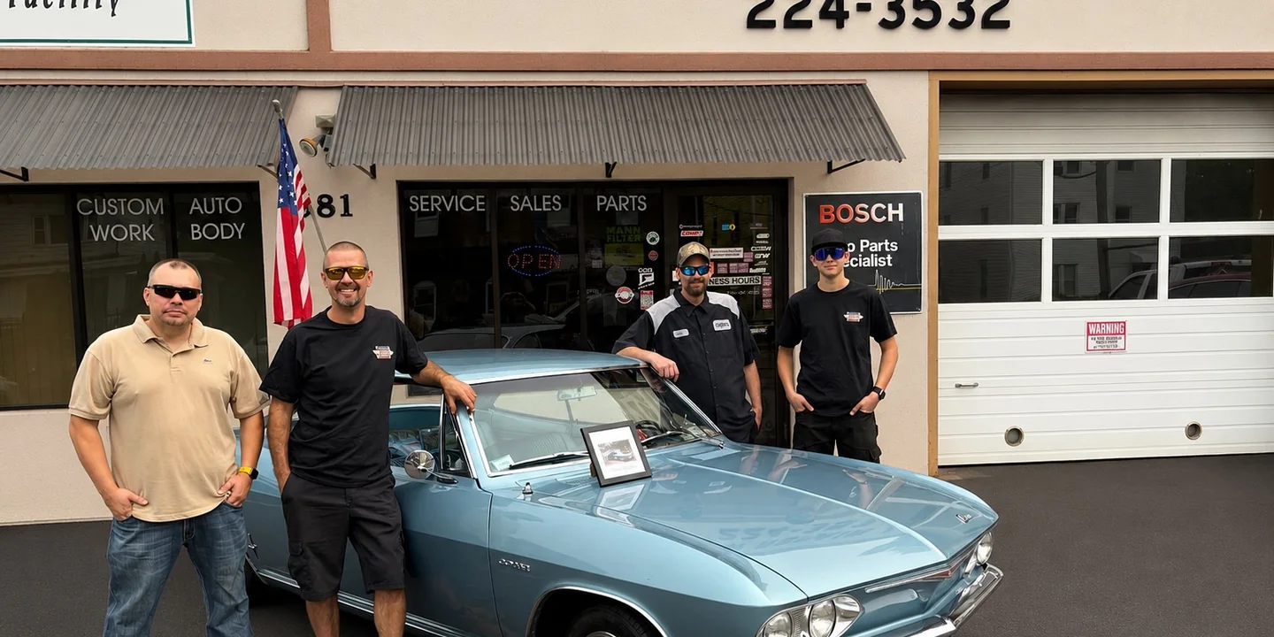 The Ceglarz Motor Repair & Sales team standing in front of the shop at 581 W Main St with a classic light-blue Chevrolet Corvair